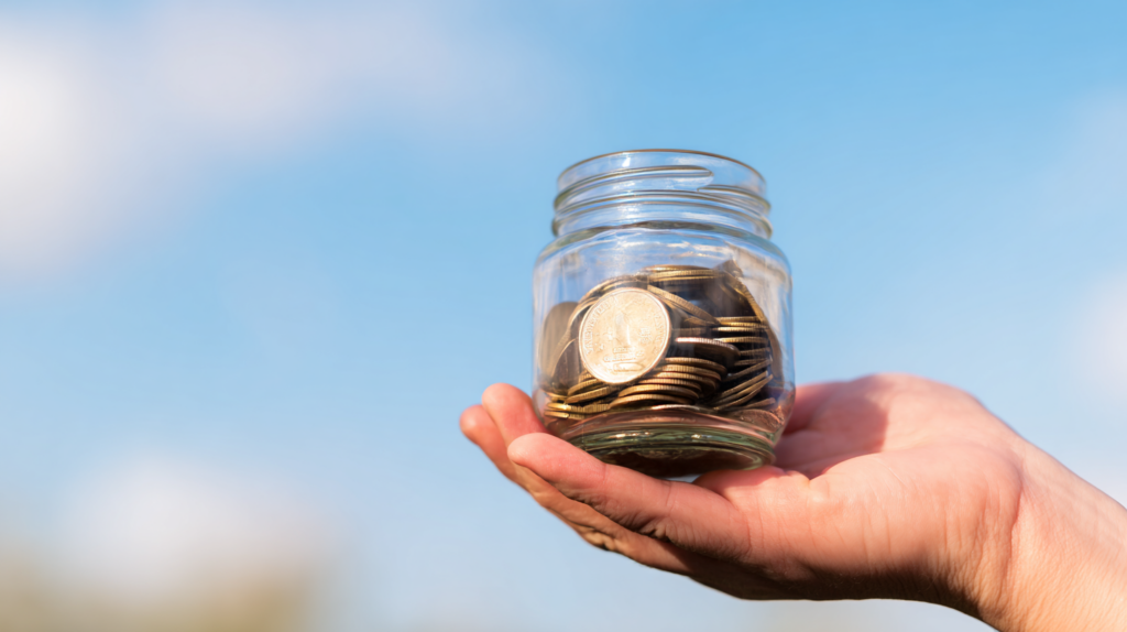 hand holding a jar piggy bank filled with coins
